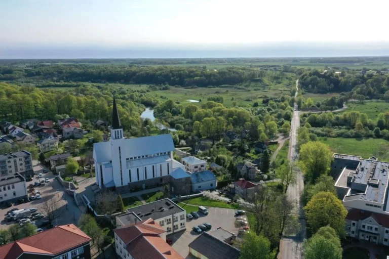 Aerial view of a white church with a tall black steeple in a green riverside town.