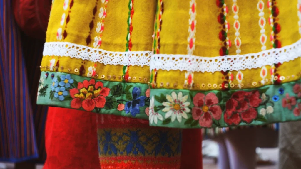 A close-up of vibrant floral embroidery and lace on a traditional yellow folk-style skirt.