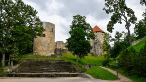 Ancient stone towers of the Cēsis medieval castle ruins in Latvia under a dramatic cloudy sky.