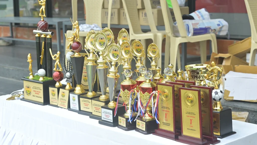 A variety of gold and silver sports trophies and plaques arranged on a white clothed table.