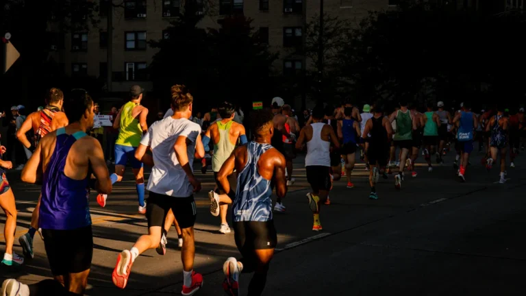 A group of marathon runners silhouetted against the golden morning sun as they run through city streets.