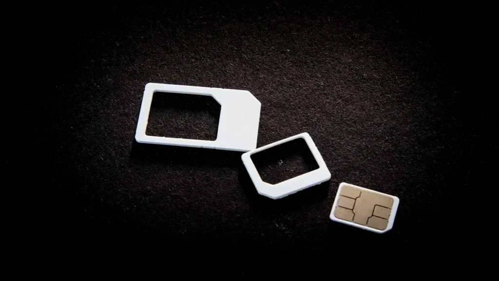 A close-up of a mobile SIM card and its various adapter frames on a dark, textured background.