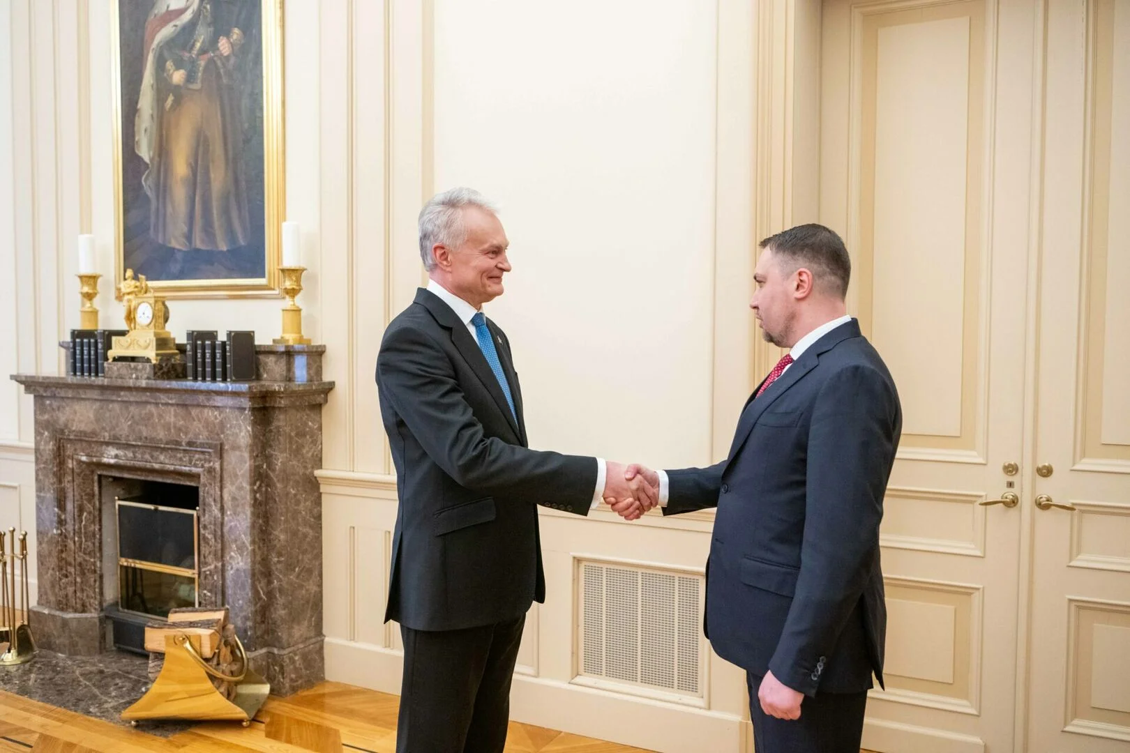 President Gitanas Nausėda shaking hands with Kyrylo Budanov in a formal room with a fireplace.