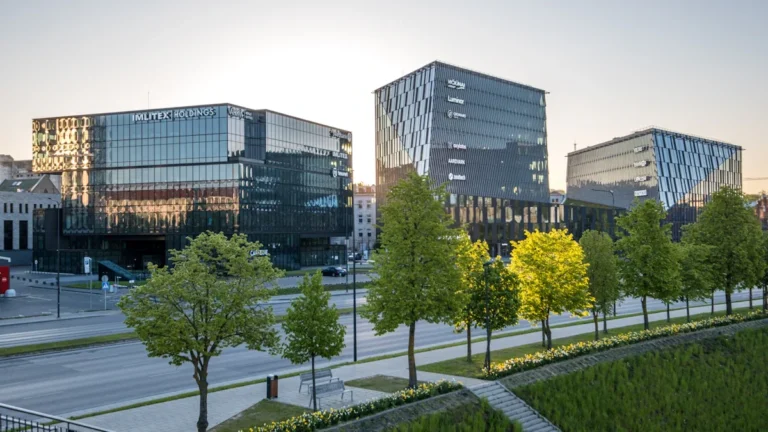 Modern glass-fronted office buildings in a Lithuanian business district during the early evening.