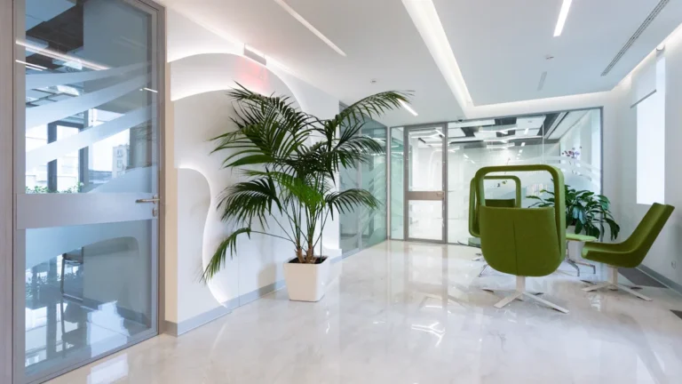 Modern clinic waiting area with sleek white floors, glass doors, and comfortable green seating.