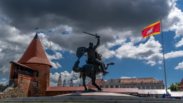 The Vytis knight statue and a waving Lithuanian flag in front of historical fortifications, symbolizing national defense.