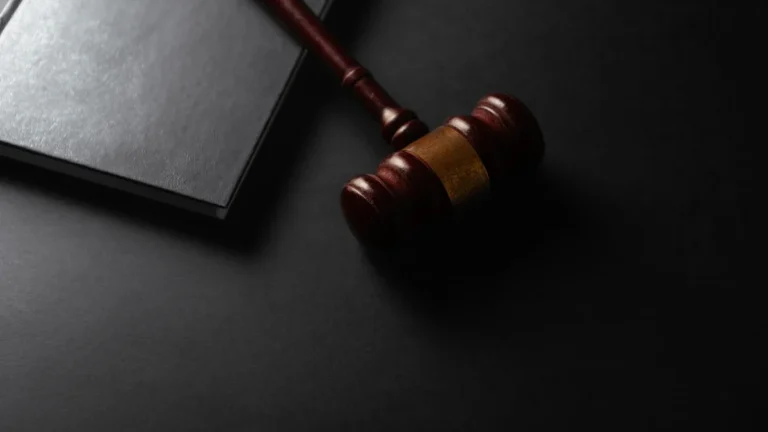 A wooden judge's gavel rests on a black law book against a dark, minimalist background.