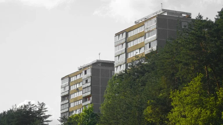 A brown and white multi-story apartment building in Vilnius, Lithuania, framed by green trees.