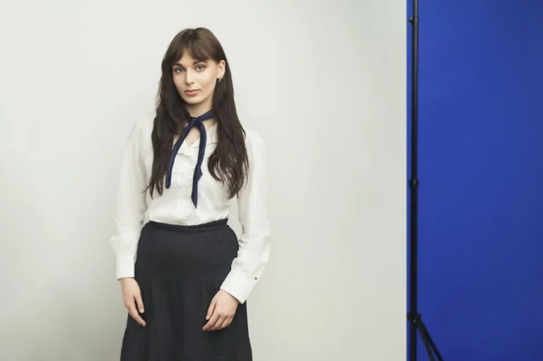 Woman with dark hair wearing a white blouse and blue scarf against a studio background.