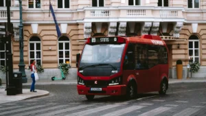 A modern red public transport bus with destination signage drives through a city square in Vilnius.