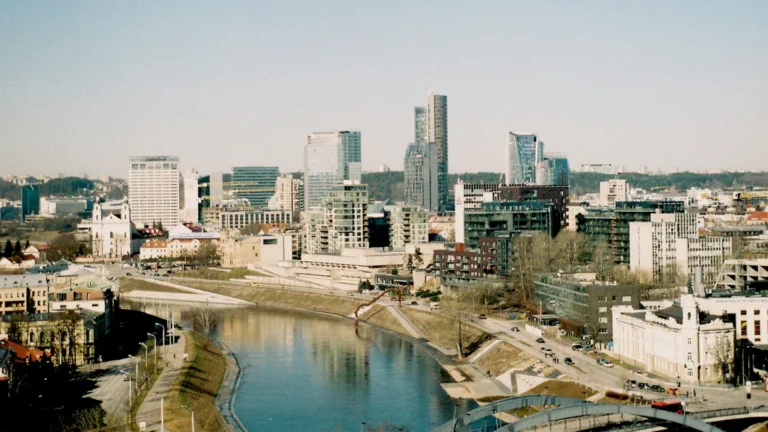A wide shot of the Vilnius city skyline in Lithuania, showcasing modern skyscrapers alongside the Neris River.