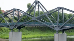 A modern grey metal truss bridge spanning a river with a building in the background in Lithuania.