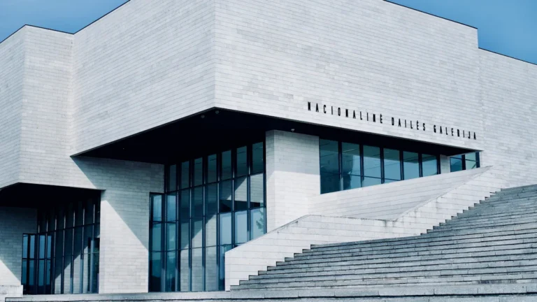 A modern white concrete institutional building in Lithuania with wide stone steps under a clear blue sky.