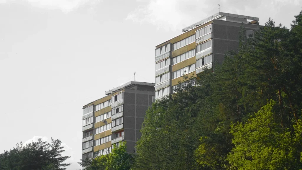 Several multi-story residential apartment blocks in Vilnius, Lithuania, partially obscured by green pine trees.