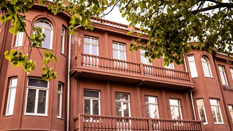 A classical terracotta-colored residential building with balconies and green trees in Lithuania.