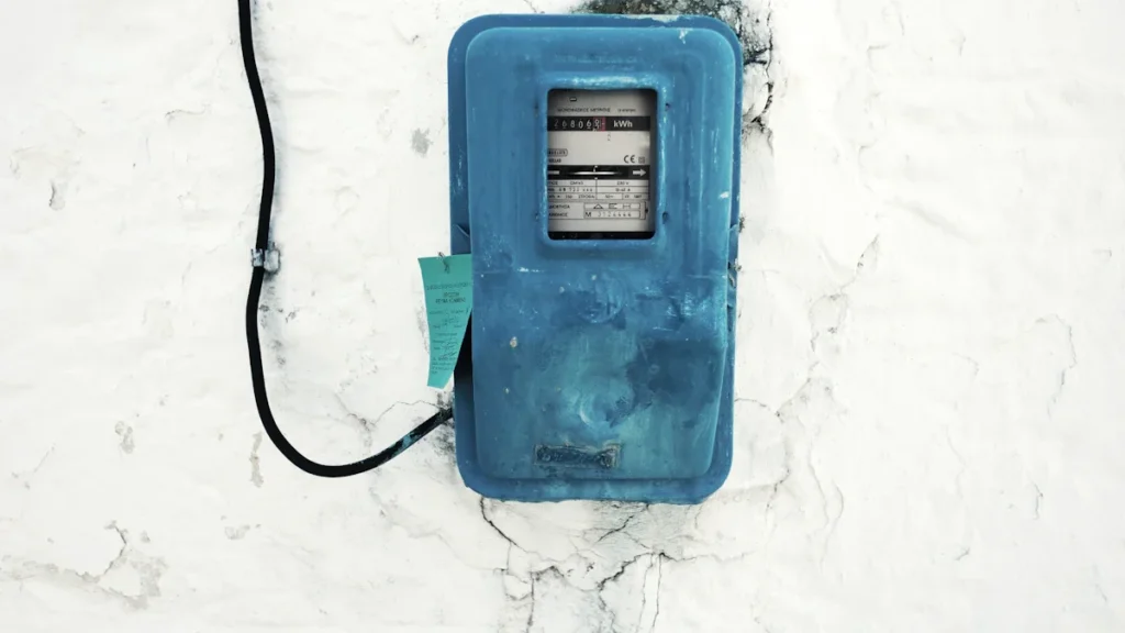 A blue analog electricity meter mounted on a weathered white wall in a residential building.