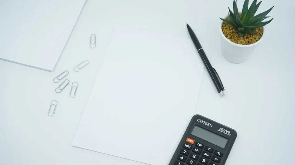 A black calculator and pen beside blank white paper on a clean office desk.
