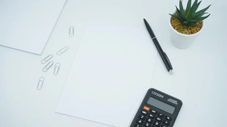 A black calculator and pen beside blank white paper on a clean office desk.