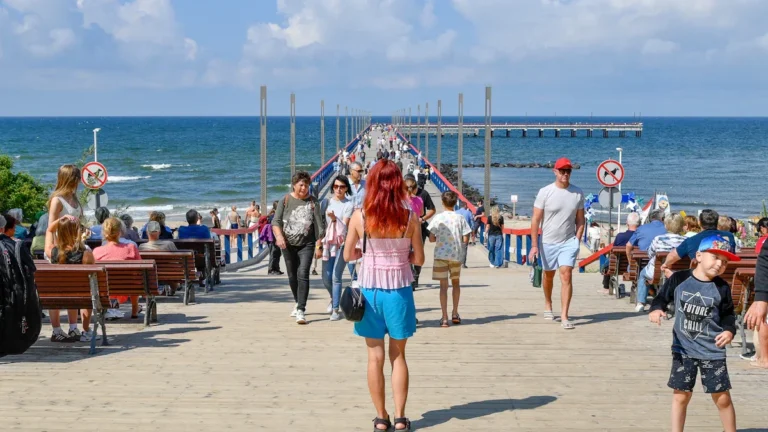 A diverse crowd of people and families walking on the iconic Palanga Bridge overlooking the Baltic Sea in Lithuania.