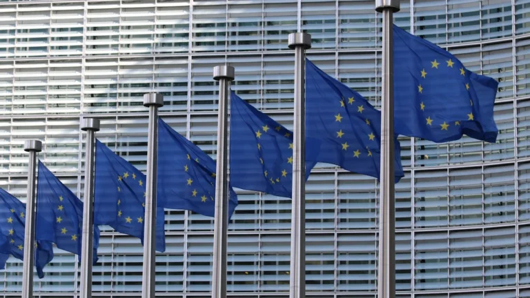 A row of blue European Union flags waving in front of the Berlaymont building in Brussels.