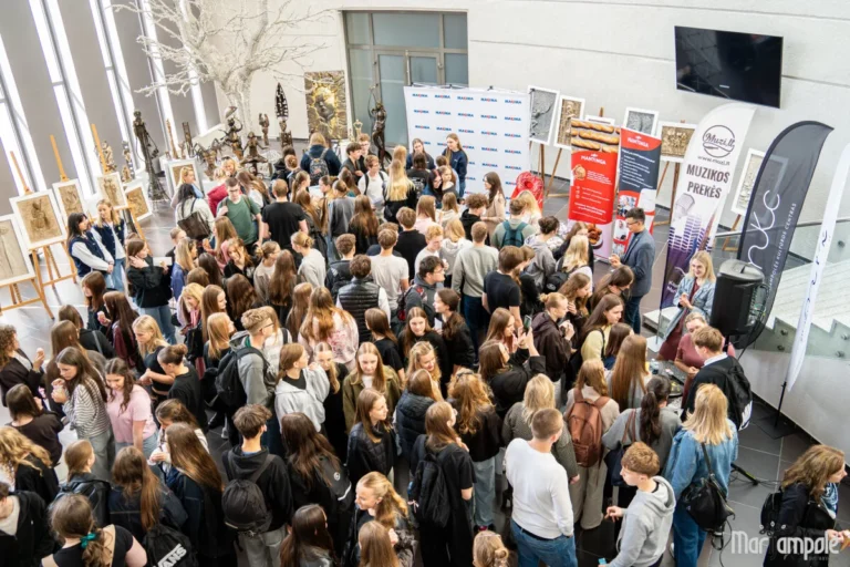 A large crowd of students gathers in a spacious hall featuring informational banners and displayed artwork.