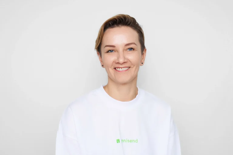 A smiling woman with short blonde hair and blue eyes wearing a white branded sweatshirt.