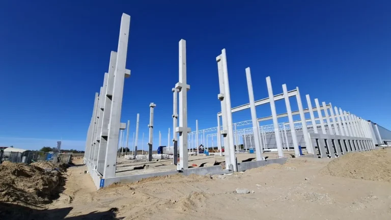 Tall concrete pillars form the structural skeleton of a large new building under clear skies.