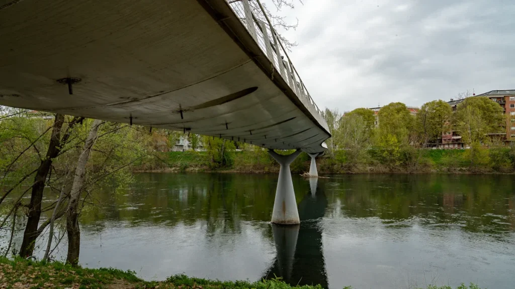 A wide shot of a modern concrete bridge crossing a calm river surrounded by green trees.