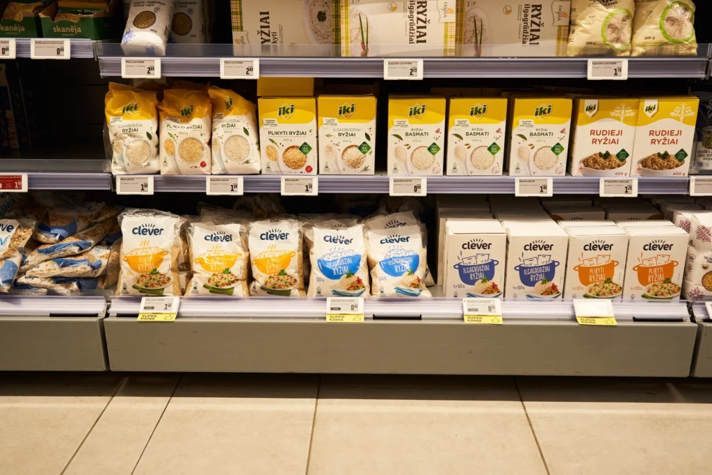 Supermarket shelves stocked with various brands of packaged rice in bags and boxes with price tags.