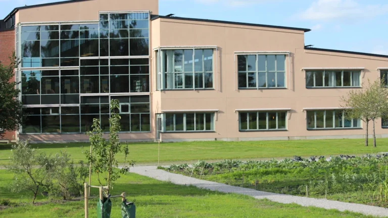 A modern university building overlooking organized agricultural garden plots used for training and research.