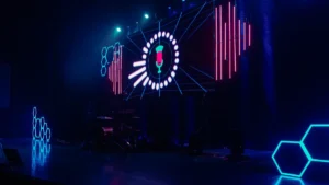 A modern event stage with neon blue lights and a digital microphone icon on screen.