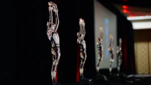 Several clear glass award statuettes shaped like human figures stand in a row under event lighting.