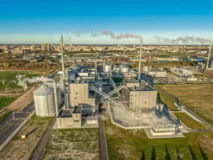 Aerial view of a large industrial factory with silos and smokestacks emitting white steam.