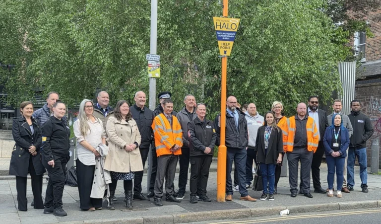 A group of people standing outdoors beside a yellow Operation Halo emergency help point sign.