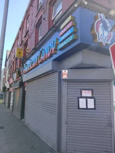 A closed storefront with metal shutters down, featuring American Candy signage and posted legal notices.