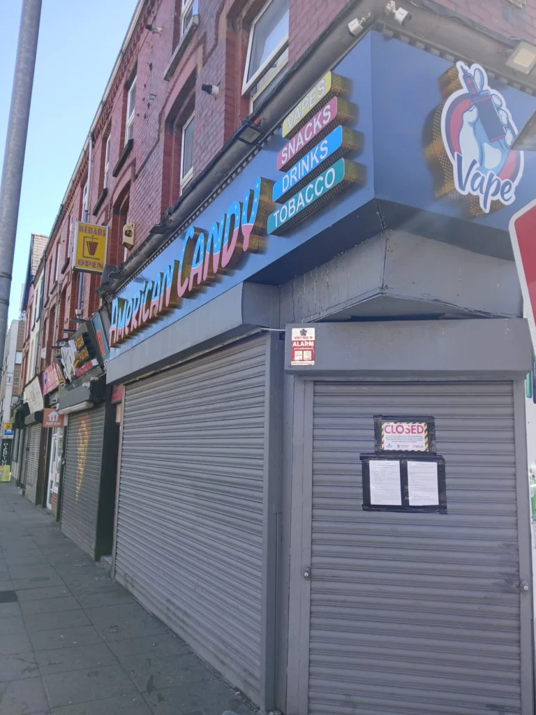 A closed storefront with metal shutters down, featuring American Candy signage and posted legal notices.