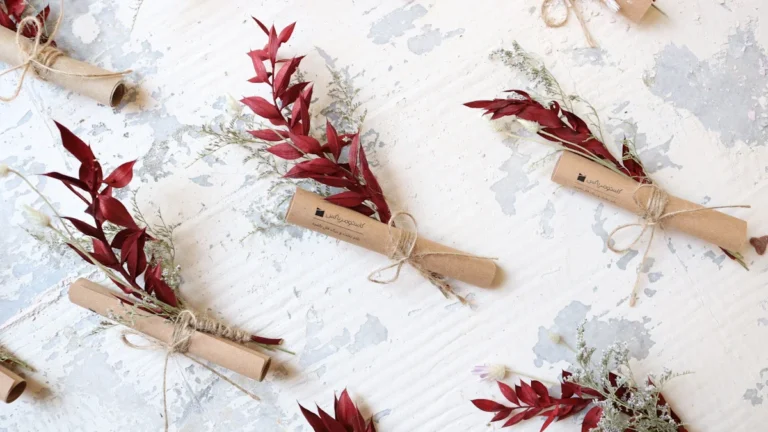 Several small paper scrolls tied with twine and red floral sprigs on a white textured background.