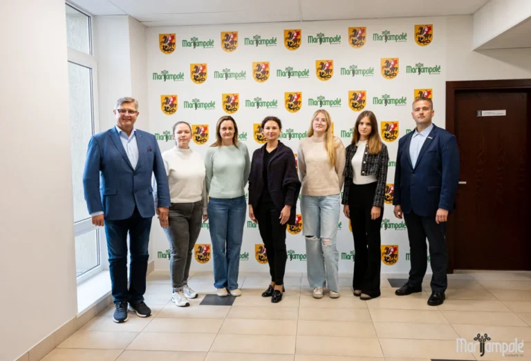 Seven people stand in a line in front of a wall with repeated city logos.