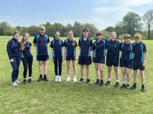 Ten school students posing in matching blue sports uniforms on a large green grass field.