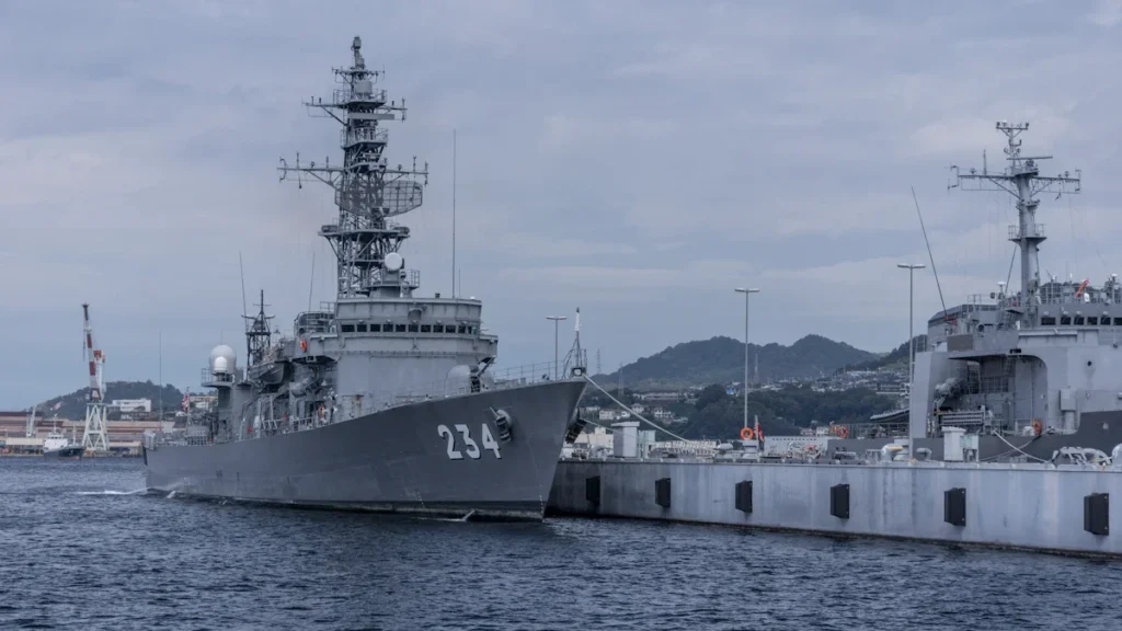 A grey naval destroyer docked at a pier, showcasing its radar masts and superstructure.
