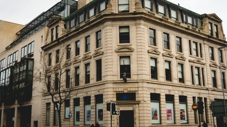 A grand multi-story stone building on a street corner with modern glass architecture on top.