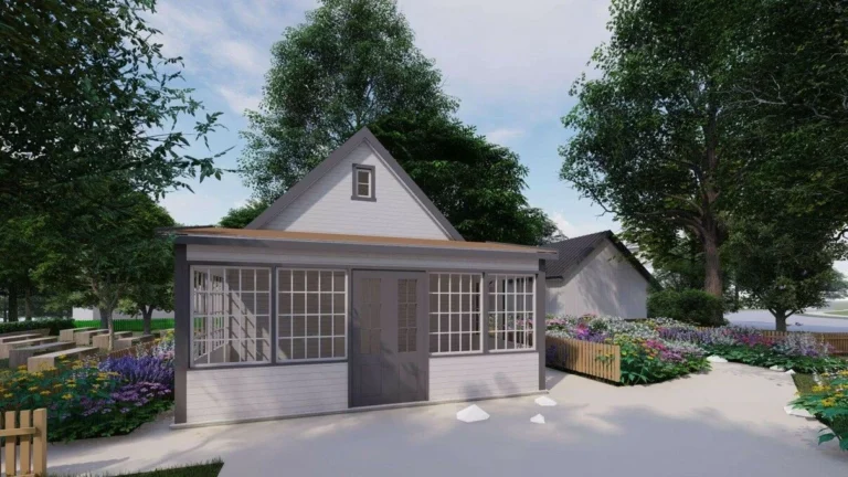 Small white garden studio with large grid windows and dark doors surrounded by colorful flower beds.