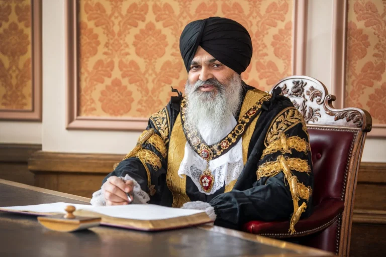 A man with a black turban and ceremonial robes signing a ledger at a desk.