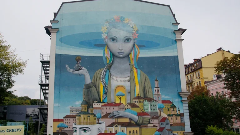 A massive blue mural of a figure with a flower crown overlooking a painted cityscape.