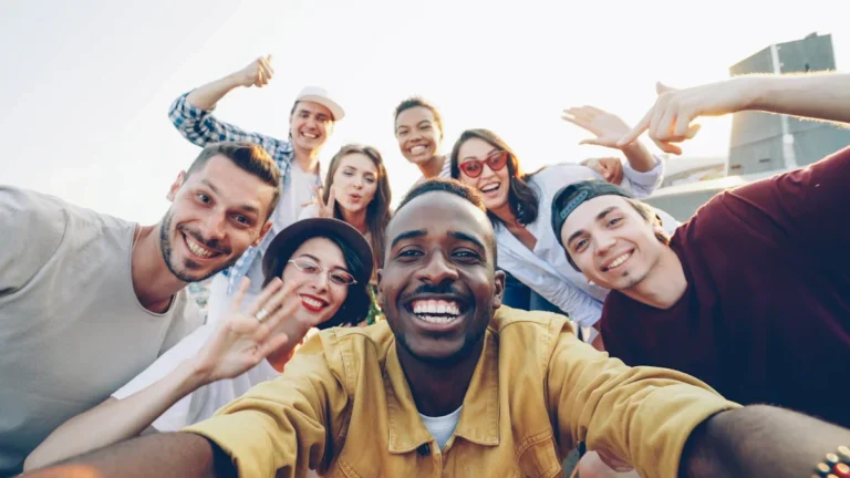 A diverse group of smiling people from various ethnic backgrounds taking a group selfie together outdoors.