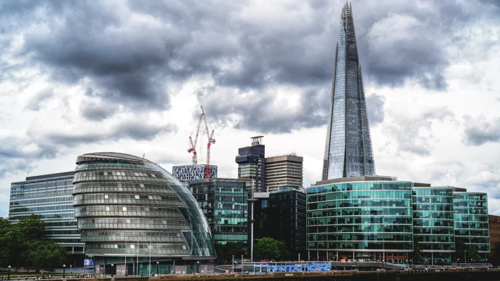 The London skyline featuring the Shard and City Hall building against a dramatic cloudy sky.