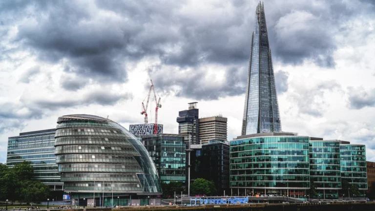 The London skyline featuring the Shard and City Hall building against a dramatic cloudy sky.
