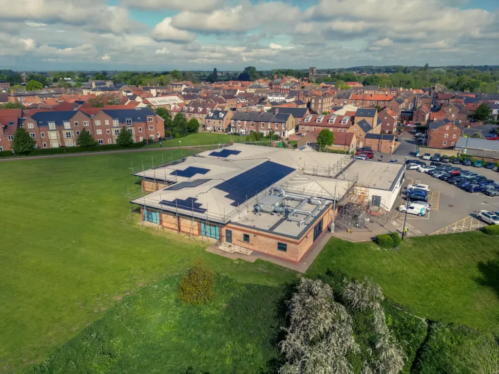 Aerial view of a commercial building with solar panels surrounded by green fields.