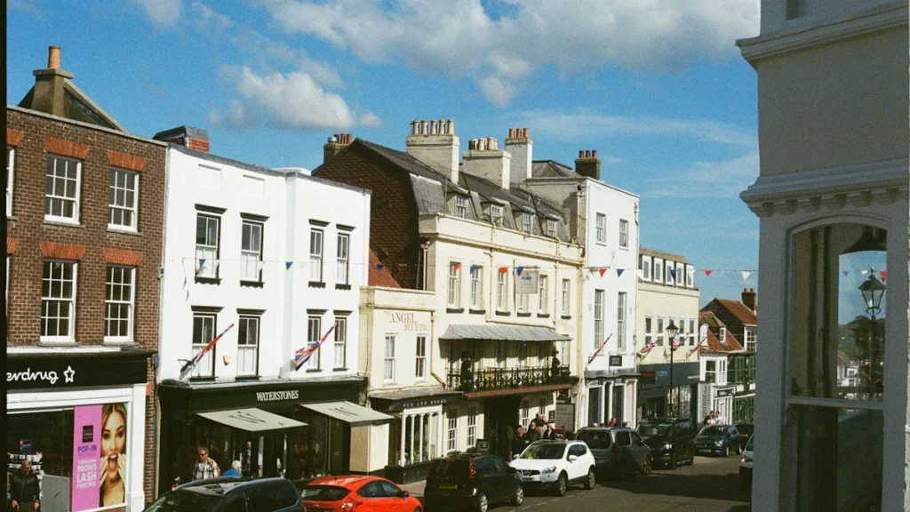 A bright, sunny street scene in an English town with classic architecture and parked cars.