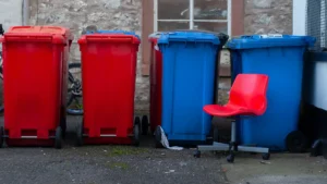 A row of red and blue domestic wheelie bins standing against a stone wall.